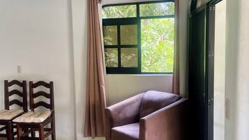 Una habitación con cama, una silla, una mesa y una ventana con cortinas.