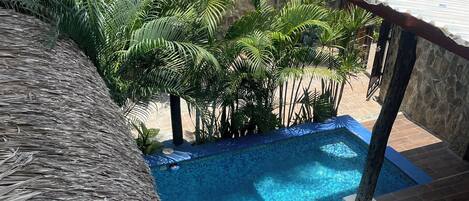 A clear blue swimming pool with a thatched roof and palm trees in the background.
