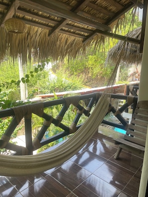 Una hamaca colgada de una estructura de madera con techo de paja, con vista a un paisaje verde y exuberante.