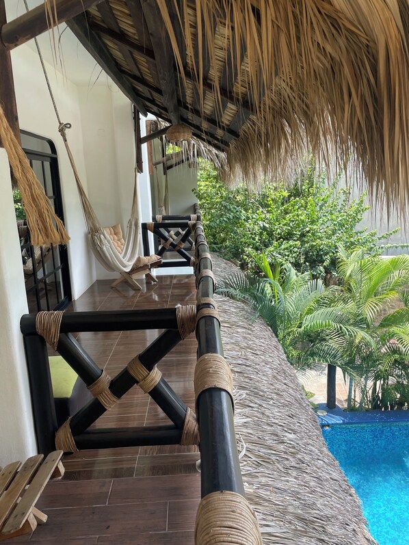 Una silla hamaca, una piscina y una estructura de techo de paja.