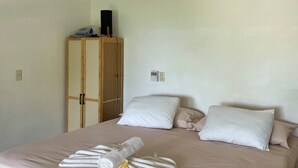 A hotel room with a bed, pillows, a ceiling fan, an air conditioning unit, and a wooden wardrobe. - Villa del Mar (San Pedro Pochutla)