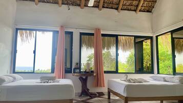 A hotel room with two beds, a ceiling fan, large windows with curtains, and a view of the sea.