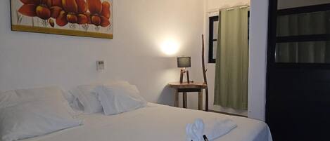 Una habitación de hotel con una cama bien hecha, un cuadro en la pared, una lámpara en una mesita de noche y una ventana con cortinas.