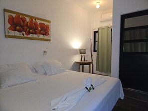 Una habitación de hotel con una cama bien hecha, un cuadro en la pared, una lámpara en una mesita de noche y una ventana con cortinas.