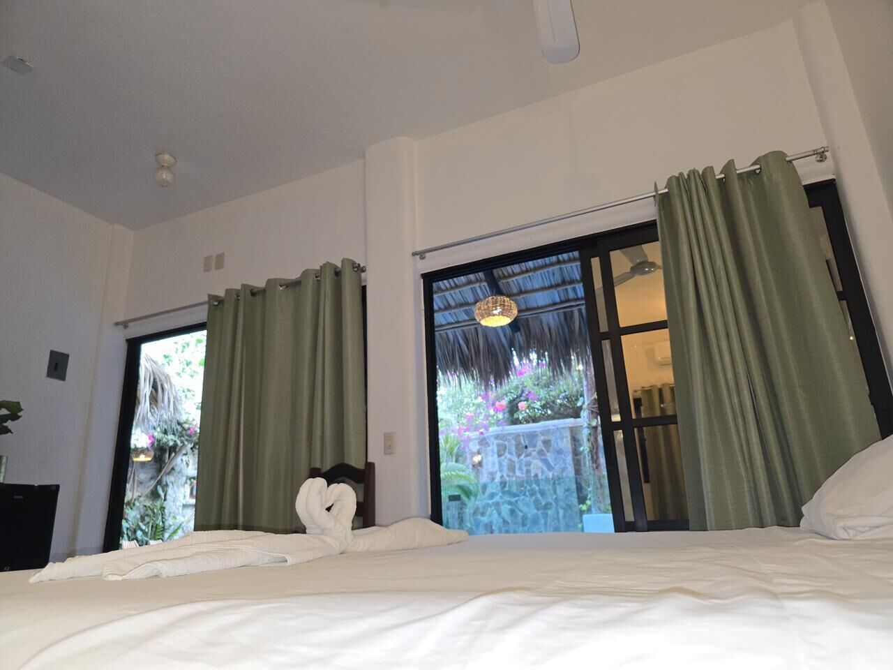 Une chambre d’hôtel avec un lit, des rideaux, une fenêtre et une vue sur la verdure environnante.
