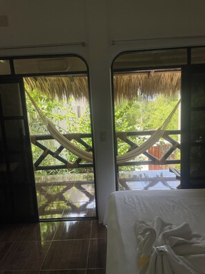 A room with a bed, a window with a view of greenery, and a hammock outside. - Villa del Mar (San Pedro Pochutla)