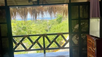 Ein Hotelzimmer mit Bett, einem Schreibtisch, einem Fernseher und einem Balkon mit Blick auf Grünflächen.