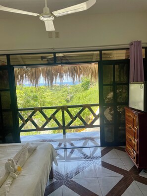 Habitación de hotel con cama, cómoda, televisor y balcón con vista a zonas verdes.