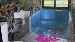A bathroom with a stone wall, a white sink, a white toilet, and a blue tiled bathtub. - Villa del Mar (San Pedro Pochutla)