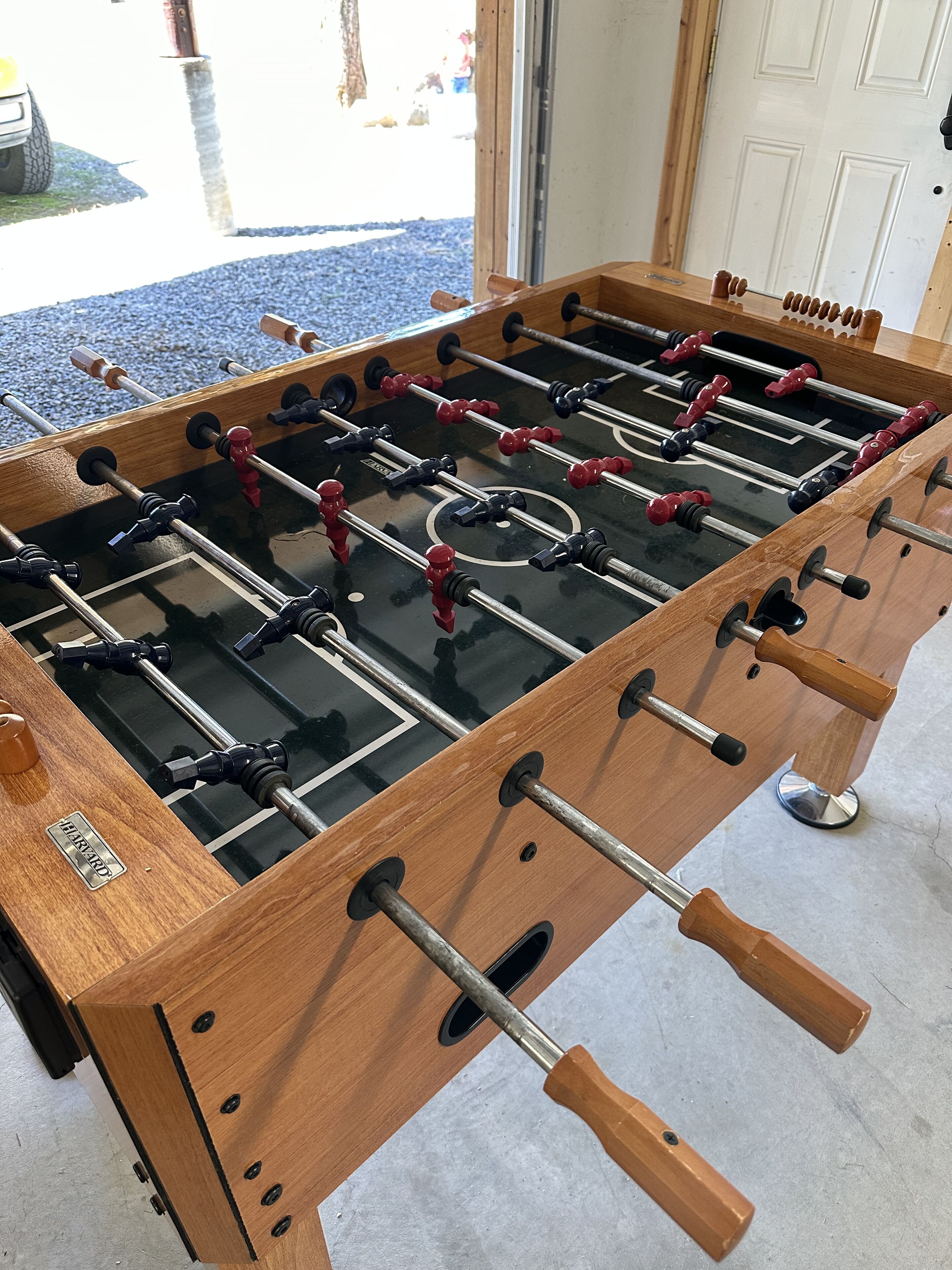 A wooden foosball table with metal rods and red and black handles.
