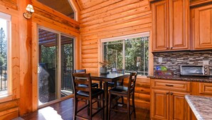 A wooden cabin interior with a dining table, chairs, a kitchen with a microwave, and a sliding glass door leading outside. - Log Cabin Getaway: WIFI, GameRoom, Firepit, pets OK! (Cascade)