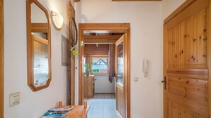 Un couloir avec des portes en bois, une table à manger avec des magazines, et une vue sur une pièce dotée d’une fenêtre.