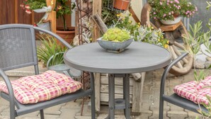 Une table ronde avec un bol en métal, deux chaises dotées de coussins à carreaux et, au fond, des plantes en pot.