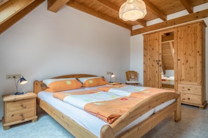 Un lit en bois avec une tête de lit, des tables de chevet, une armoire et un luminaire suspendu au plafond, dans une pièce aux murs blancs.
