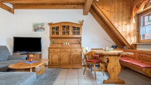 Un salon confortable avec un téléviseur, un canapé, un meuble en bois, une table à manger et un banc.