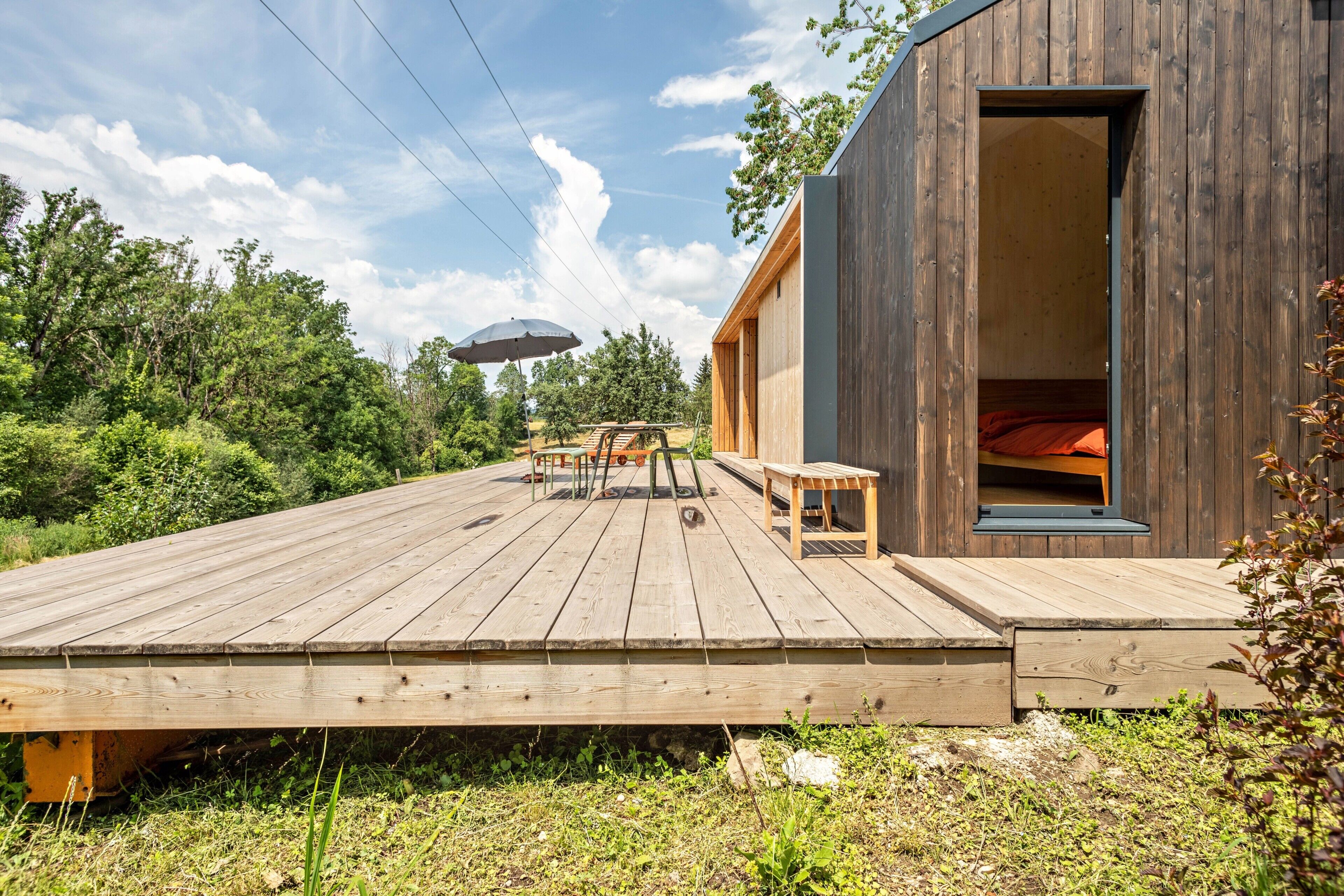 A wooden deck with outdoor furniture, a covered picnic table, and a building with an open door.