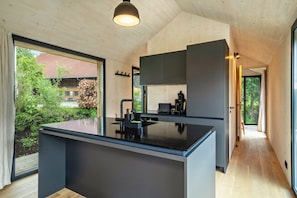 A modern kitchen with a large island, wooden flooring, and a view of the outdoors.