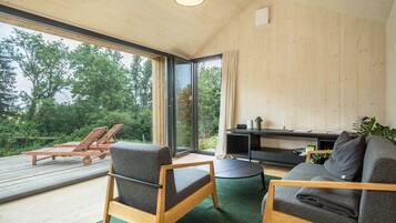 Ein modernes Interieur mit Holzbalkendecke, großen Fenstern, einer Couch, einem Sessel und einem kleinen Tisch.