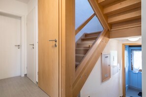 Un escalier en bois avec un puits de lumière, une porte dotée d’une poignée et une boîte électrique fixée au mur.