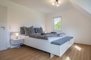 Un dormitorio moderno con cama, mesita de noche, lámpara y ventana con vistas.