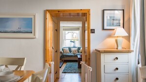 A hallway leading to a bedroom with a bed, a dresser, and a lamp.