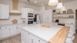 A modern kitchen with white cabinetry, a wooden island, and pendant lighting. - Heated Pool ~ Sleeps 20 ~ HUGE Family Resort Oasis (Lake Havasu City)