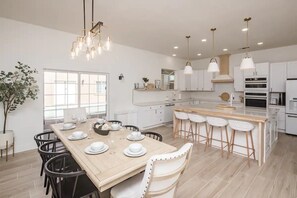 Uma cozinha moderna com armários brancos, uma ilha central com banquetas e iluminação pendente.
