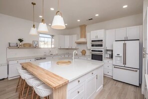 Une cuisine moderne avec des meubles blancs, un îlot central en bois doté d’un évier, des luminaires suspendus et un four encastré.