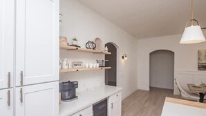 A modern kitchen with white cabinetry, a coffee station, and a dining area with a table and chairs. - Heated Pool ~ Sleeps 20 ~ HUGE Family Resort Oasis (Lake Havasu City)