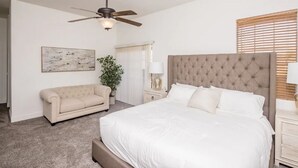 A bedroom with a large bed, a ceiling fan, a beige sofa, a nightstand with a lamp, and a window with blinds. - Heated Pool ~ Sleeps 20 ~ HUGE Family Resort Oasis (Lake Havasu City)