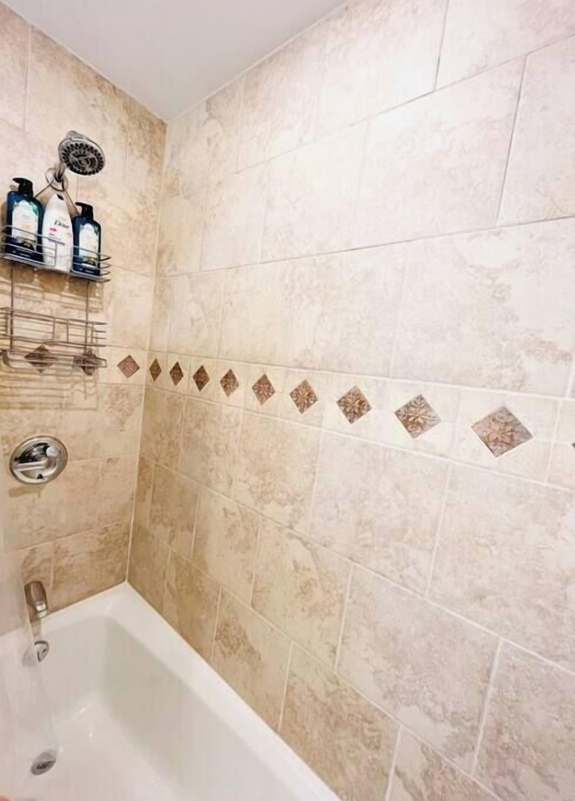 Ein Badezimmer mit beigefarbenen Fliesen, einer Dusche und einem Ablagefach mit Toilettenartikeln.