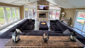 A spacious living room with a stone fireplace, large windows, and a ceiling fan. - Play @ The Hideaway - hot tub, sauna, gymnasium (Three Oaks)