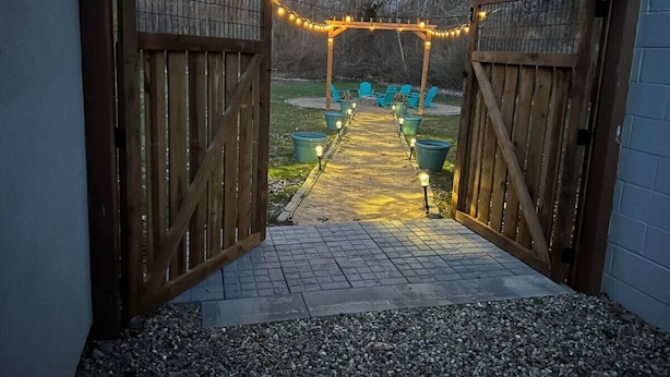 A wooden gate leading to a patio area with string lights and outdoor seating. - Play @ The Hideaway - hot tub, sauna, gymnasium (Three Oaks)