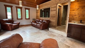 A spacious living area with leather sofas, a wooden ceiling, and a large window. - Play @ The Hideaway - hot tub, sauna, gymnasium (Three Oaks)