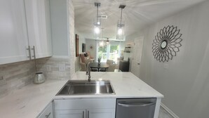 A modern kitchen with white cabinetry, a central island with a sink, and a dishwasher. There is a dining area with a table and chairs in the background.