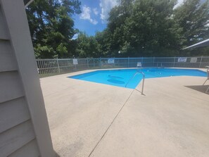 A swimming pool with a blue interior, surrounded by a concrete deck and a metal fence.