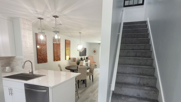 A modern kitchen with a central island, a dining area, and a staircase leading to an upper level.