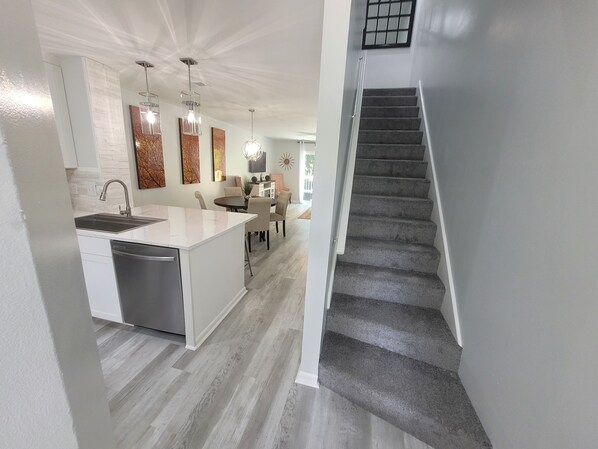 A modern kitchen with a central island, a dining area with a table and chairs, and a staircase leading to another level.