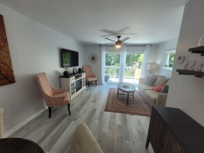 A living room with a TV, two patterned chairs, a coffee table, and a ceiling fan.