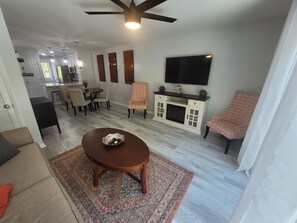 Uma sala de estar moderna com área de jantar, TV na parede e ventilador de teto.