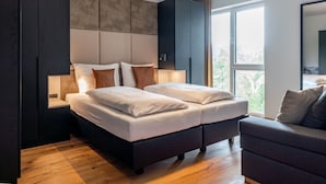 A modern bedroom with a large bed, dark wooden wardrobe, and a view of the outdoors through a large window.