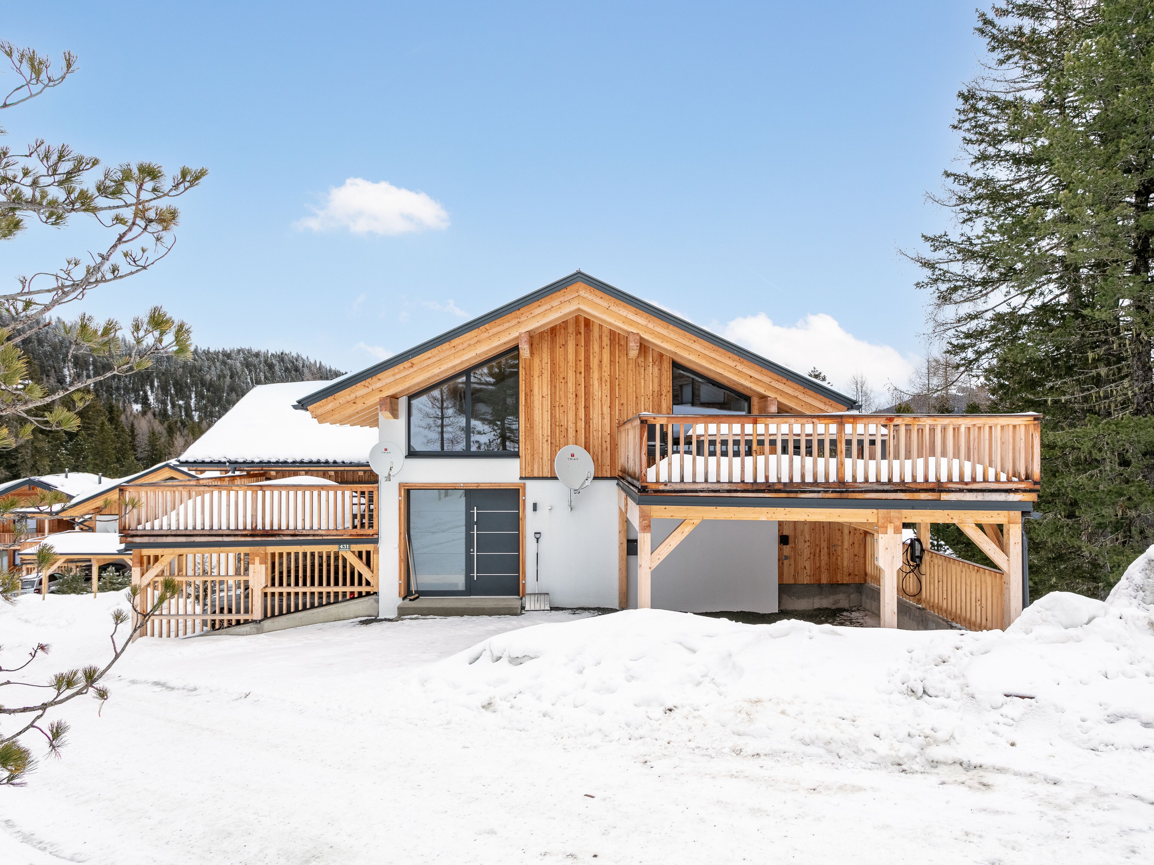 A wooden chalet with a balcony, a garage, and a snow-covered landscape.