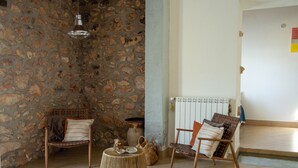 A room with a stone wall, a wicker ottoman, two wicker chairs, a hanging light fixture, and a radiator. - Villa Marianninswimming pool with hot tub in private garden (Castellammare del Golfo)