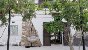 A modern outdoor seating area with a stone wall, a hanging chair, and a door leading to a covered entrance. - Villa Marianninswimming pool with hot tub in private garden (Castellammare del Golfo)
