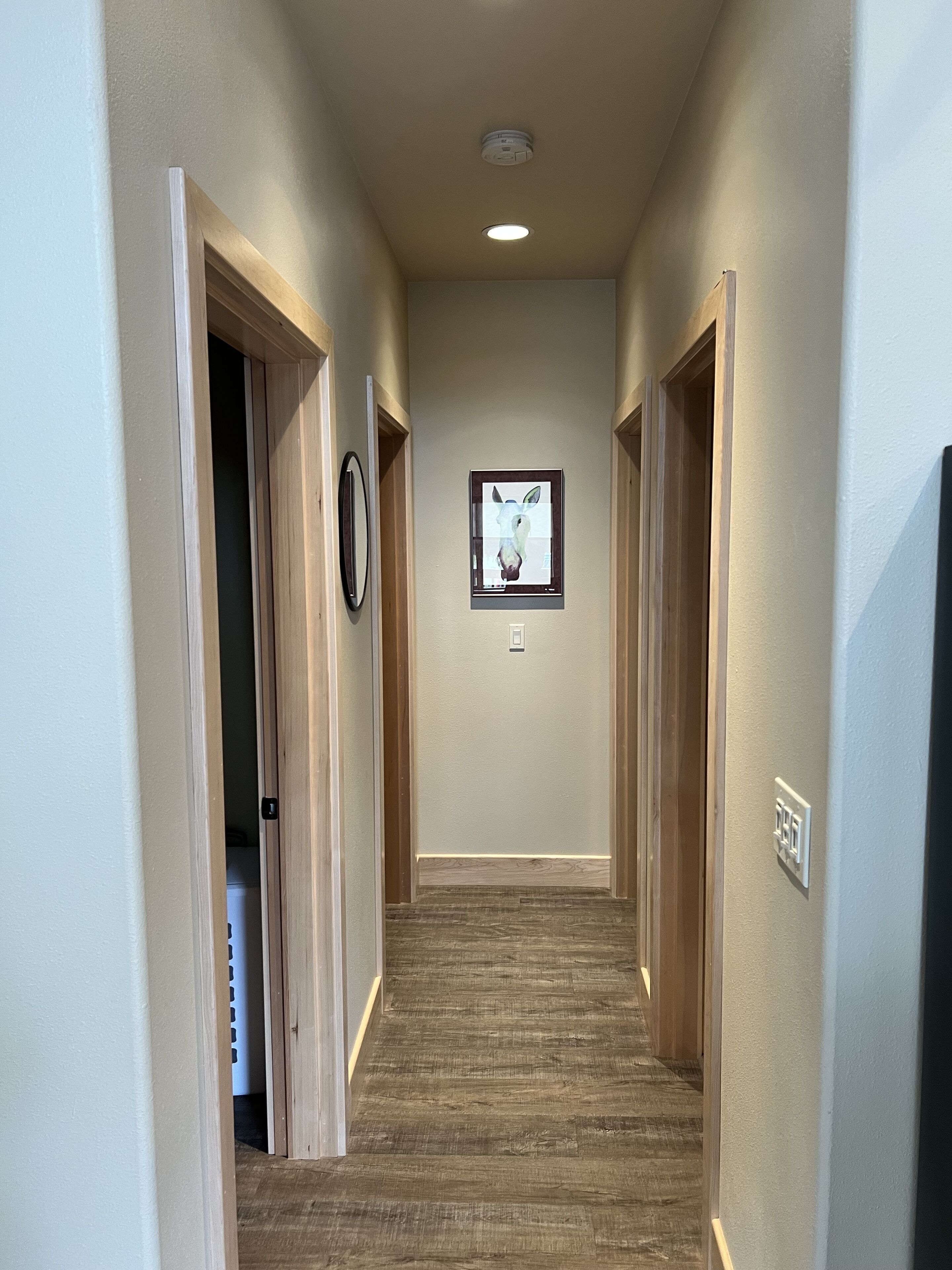 A hallway with wooden flooring, beige walls, and a framed picture on the wall.