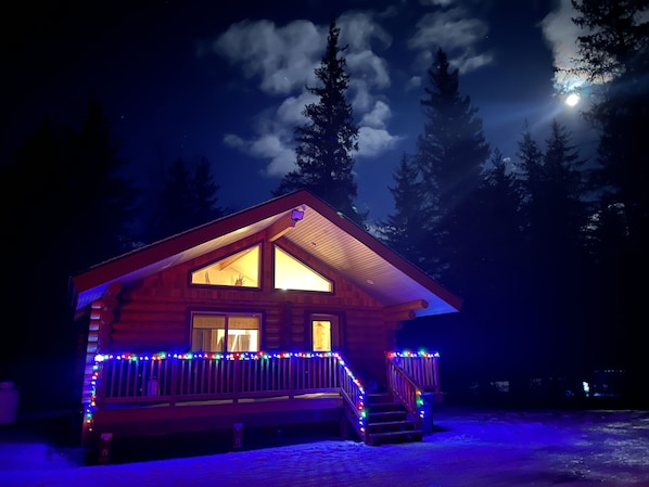 A log cabin with a porch and stairs, illuminated by string lights. - Clear creek cabin (Seward)