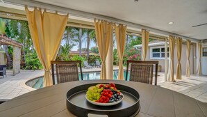 Un espace repas aménagé au bord de la piscine, avec une table dressée pour deux personnes, agrémentée d’un panier de fruits et de deux chaises en osier.