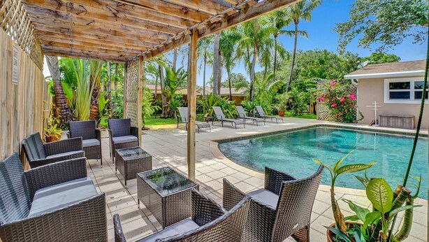 Un espace extérieur abrité, aménagé avec des meubles en osier, une piscine et des plantes tropicales.