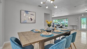 Un coin repas avec une table en bois, des chaises à l’assise rembourrée de tissu bleu et un lustre moderne.