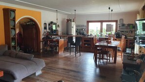 A cozy living room with a sofa and a dining area with a table and chairs. A kitchen with a refrigerator and various items is visible in the background. - House in Teichland Pool, sauna, fireplace on the Cottbus Baltic Sea with proximity to the Spreewald (Teichland)